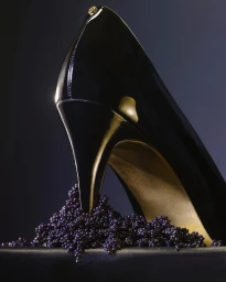 Close-up product photograph of a black patent leather stiletto high heel stepping into a dark mound of caviar.