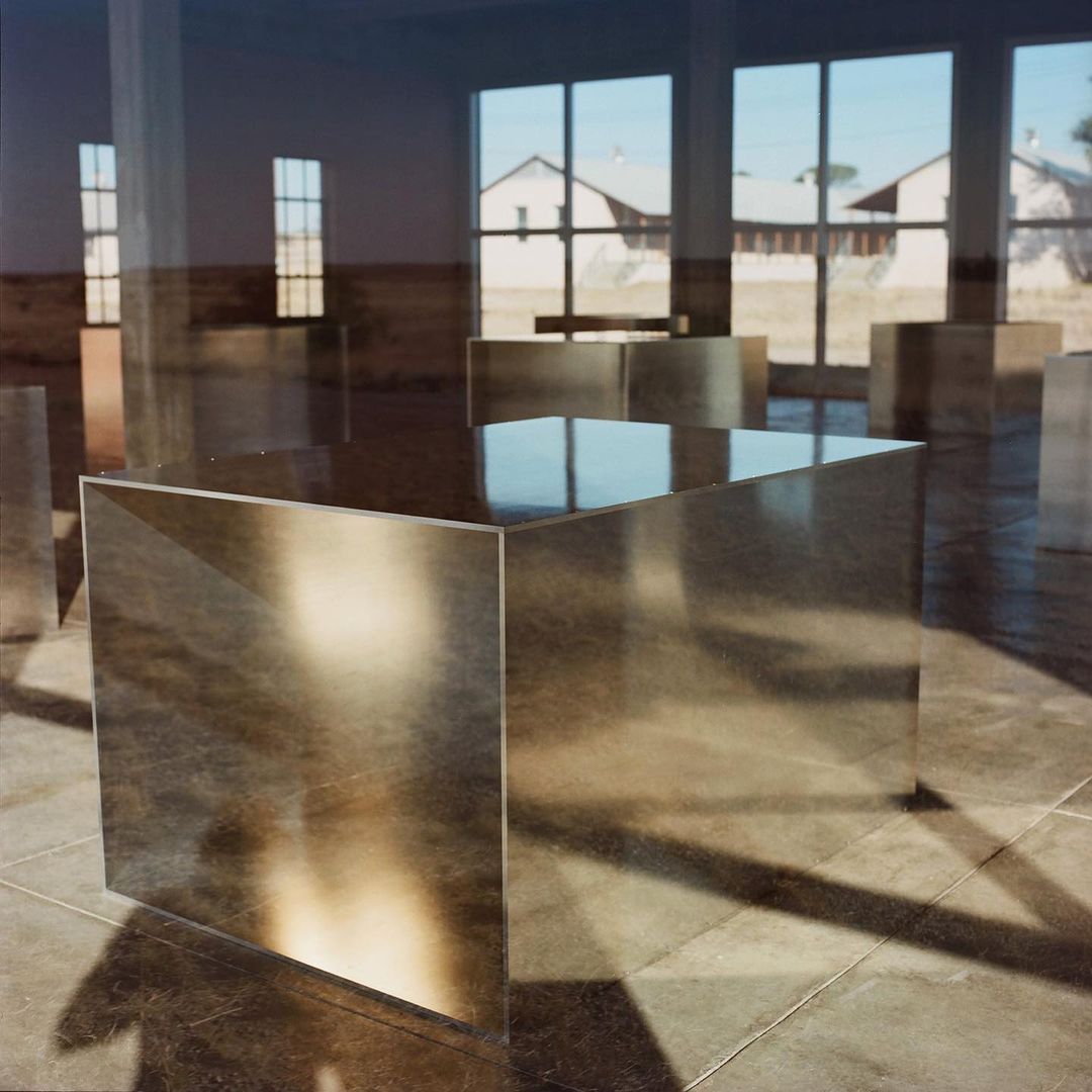Abstract art installation inside industrial space with mirror-paneled cubic sculptures, reflecting natural light from window openings.