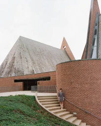 Woman in patterned dress standing on outdoor brick staircase by a modern church exterior captured by Patrick Fraser