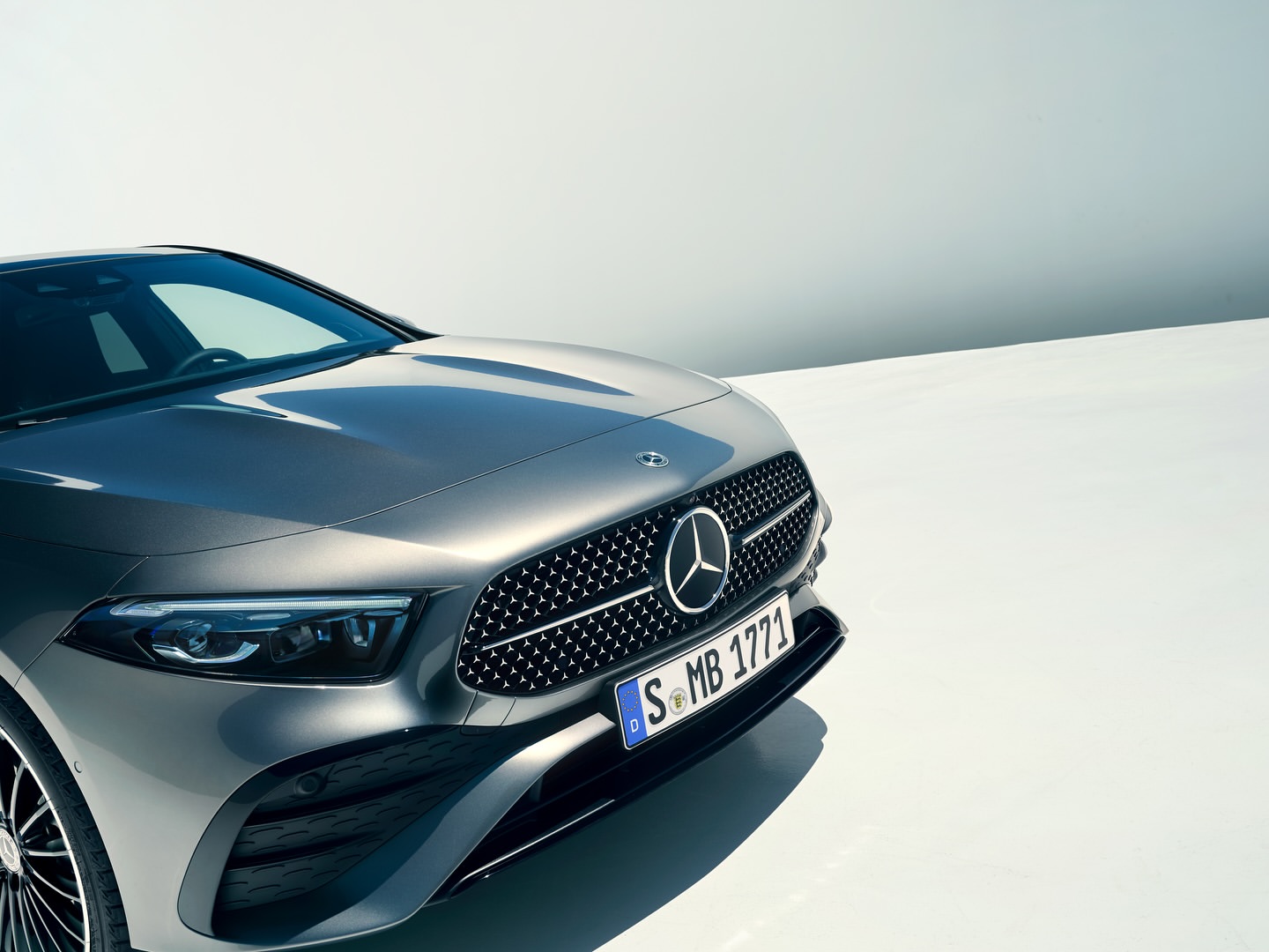 Front view of a gray Mercedes-Benz car showcasing its grille, headlights, and license plate against a bright, gradient background.