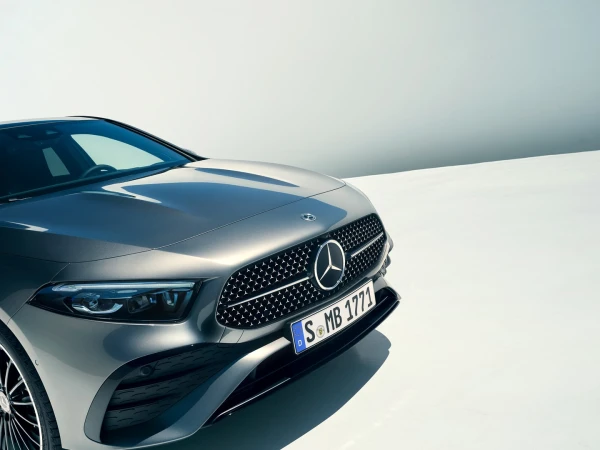 Front view of a gray Mercedes-Benz car showcasing its grille, headlights, and license plate against a bright, gradient background.