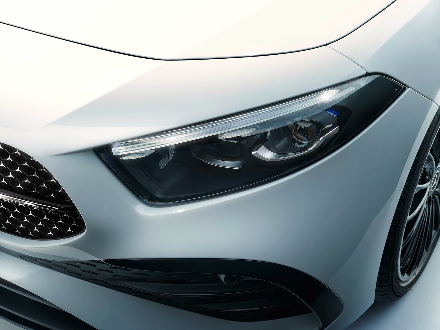 Close-up of the front of a modern white car showcasing its sleek design, headlight, grille, and partial view of the tire.