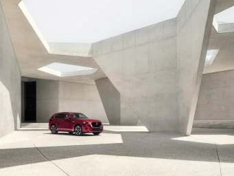Red SUV parked in a stark brutalist concrete courtyard with angular pillars and geometric skylights