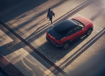 High angle aerial shot of a red crossover SUV parked on a paved lot with a woman walking past, photographed by Patrik Johall.
