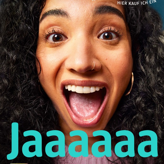 Close-up of a happy woman with curly hair, a nose ring, and a purple shirt shouting “Jaaaaaa” in a vibrant, joyful portrait.