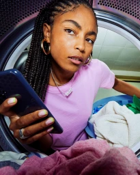Black woman in pink t-shirt holding a smartphone, viewed from inside a washing machine drum