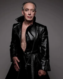 Older man wearing a glossy black leather coat with an open front against a grey backdrop