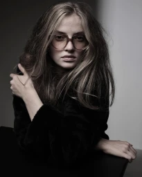 Portrait of a woman wearing tortoiseshell eyeglasses and a black textured top against a neutral studio background
