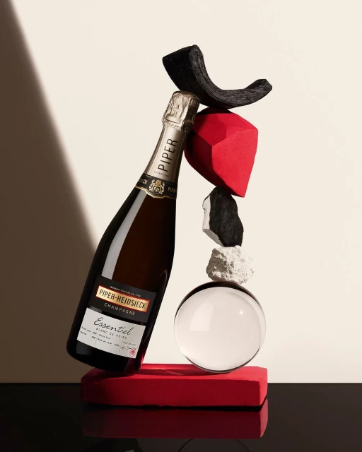 Piper-Heidsieck champagne bottle balanced on abstract shapes in a studio, casting a shadow on the cream-colored backdrop.