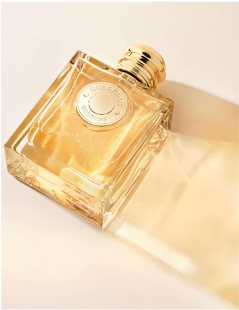 Burberry Goddess perfume bottle on its side with a transparent package, on a cream backdrop, studio lighting, and warm tones.