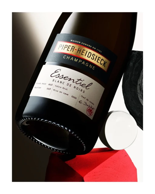 Close-up studio shot of a Piper-Heidsieck champagne bottle balanced on red, white, and black geometric blocks against a neutral background.