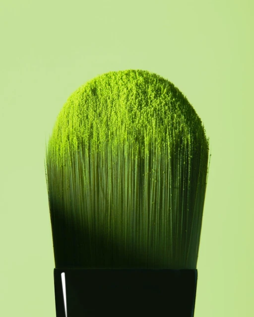 Close-up of a makeup brush densely coated with bright green powder against a soft green background, beauty concept for cosmetic product.