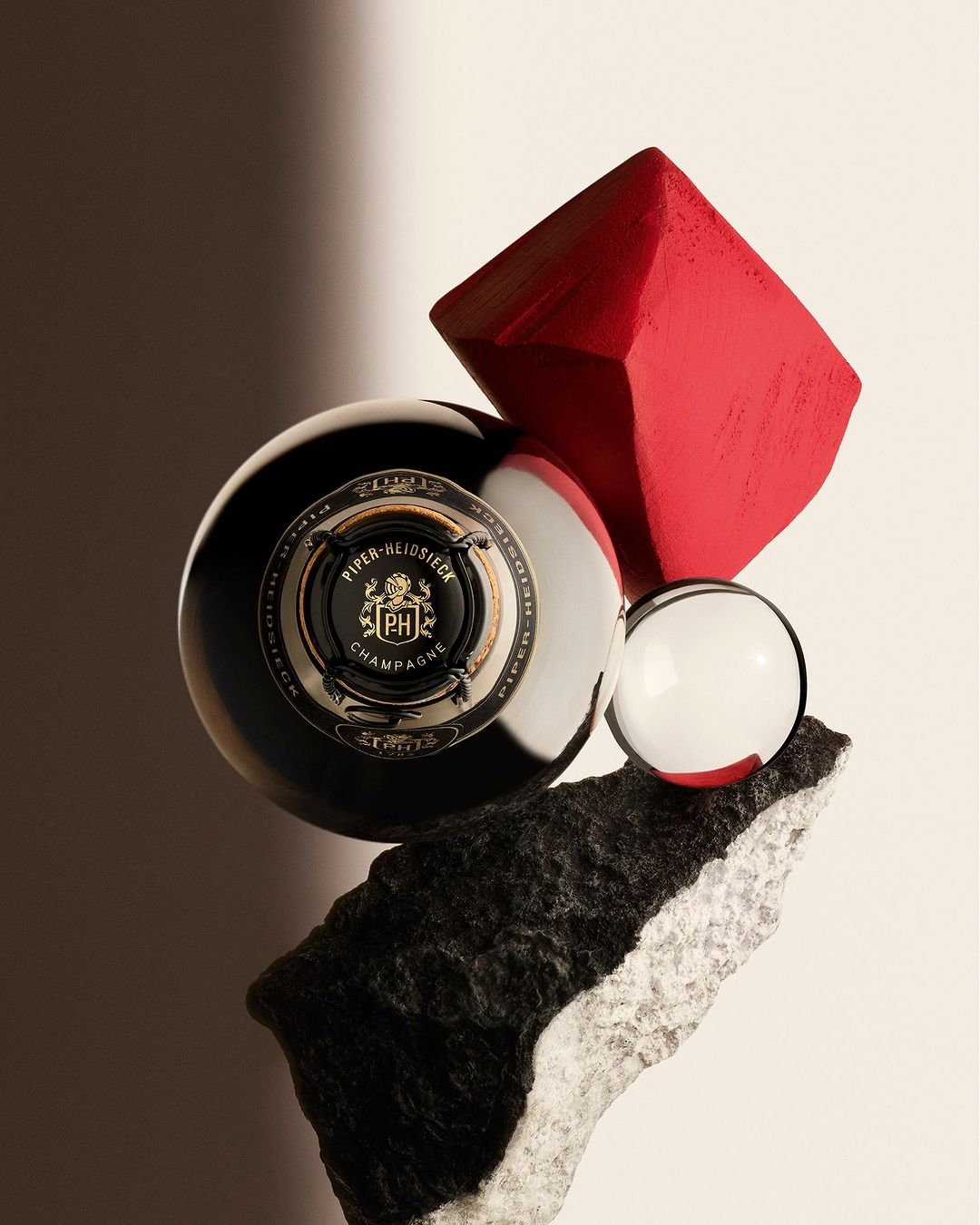 Elevated studio shot showcasing Piper-Heidsieck Champagne bottle alongside geometric shapes and textured rocks in a balanced composition.