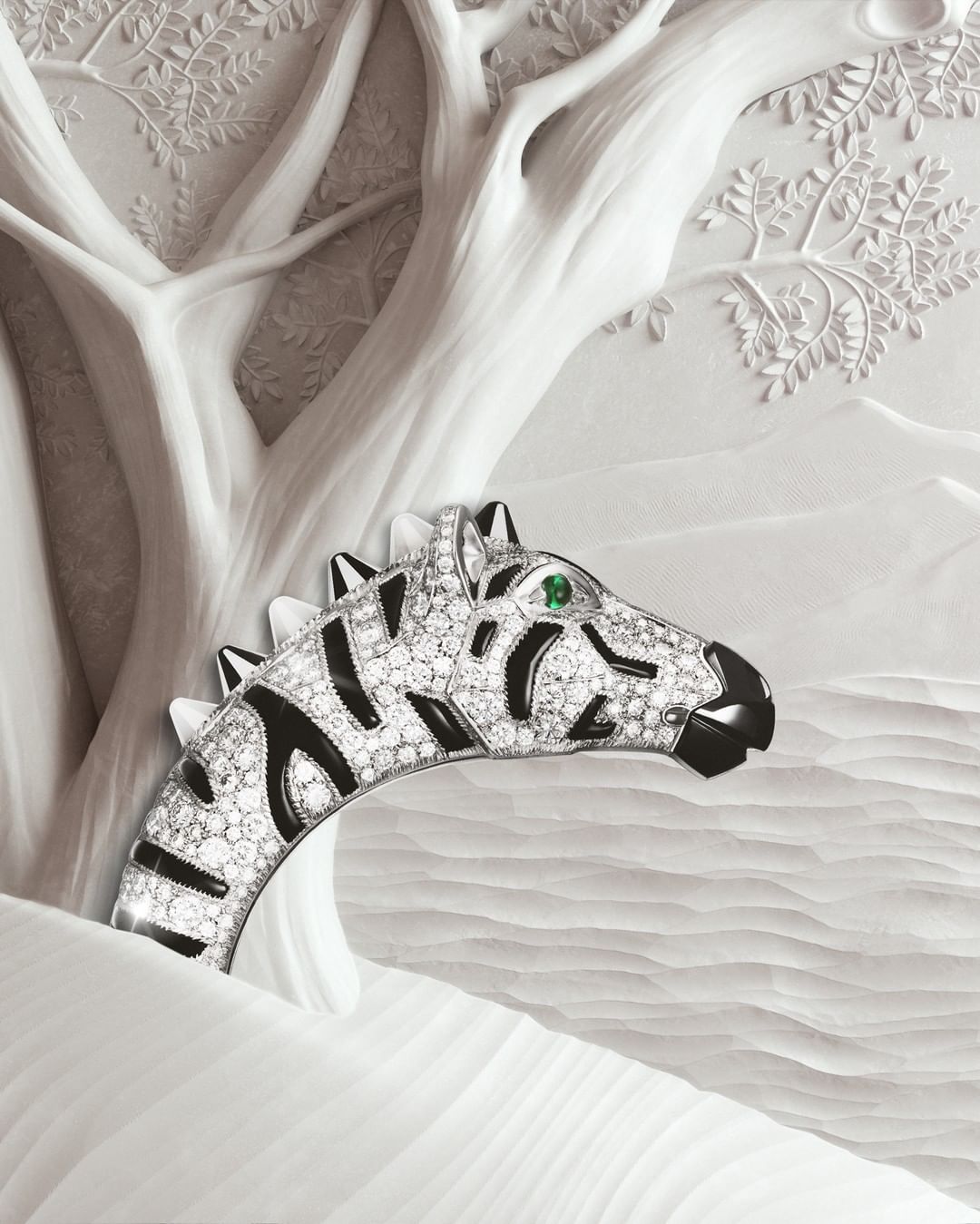 Close-up of zebra-shaped diamond bracelet with black stripes and a green emerald eye, set against a white monochromatic carved backdrop.
