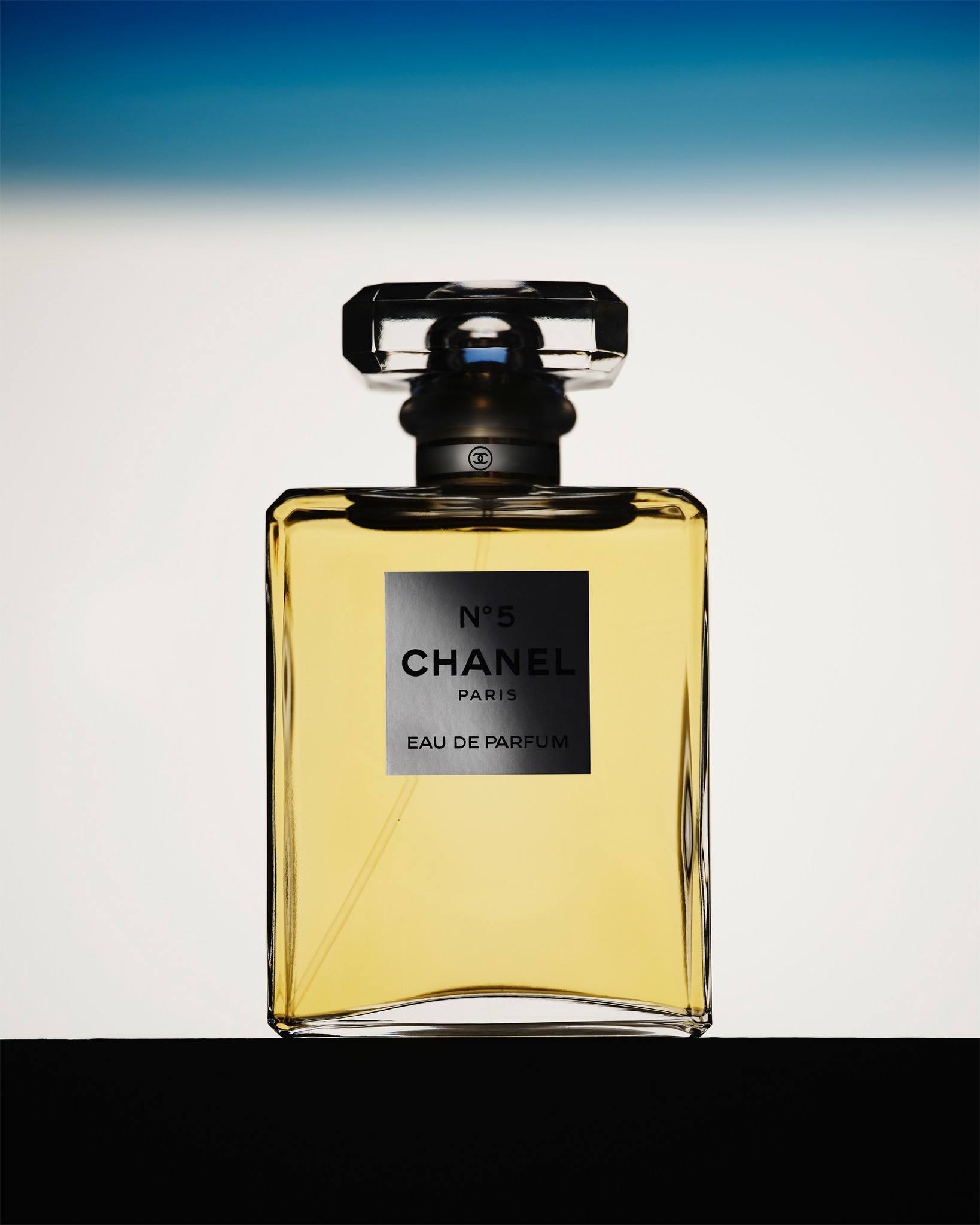 Chanel No. 5 perfume bottle presented against a gradient background. The bottle features a clear glass design and a black label.