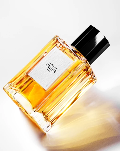 Celine perfume bottle on white background. Golden liquid with black stopper and minimalist white label with black text.