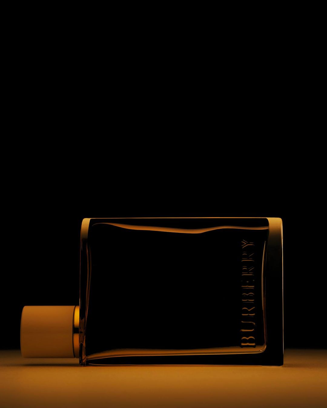 Elegant studio shot of a Burberry perfume bottle on a reflective gold surface against a dark backdrop, highlighting its sleek design.