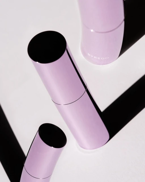 Three cylindrical lilac-colored perfume bottles with black caps, arranged diagonally on a white surface with strong shadows.