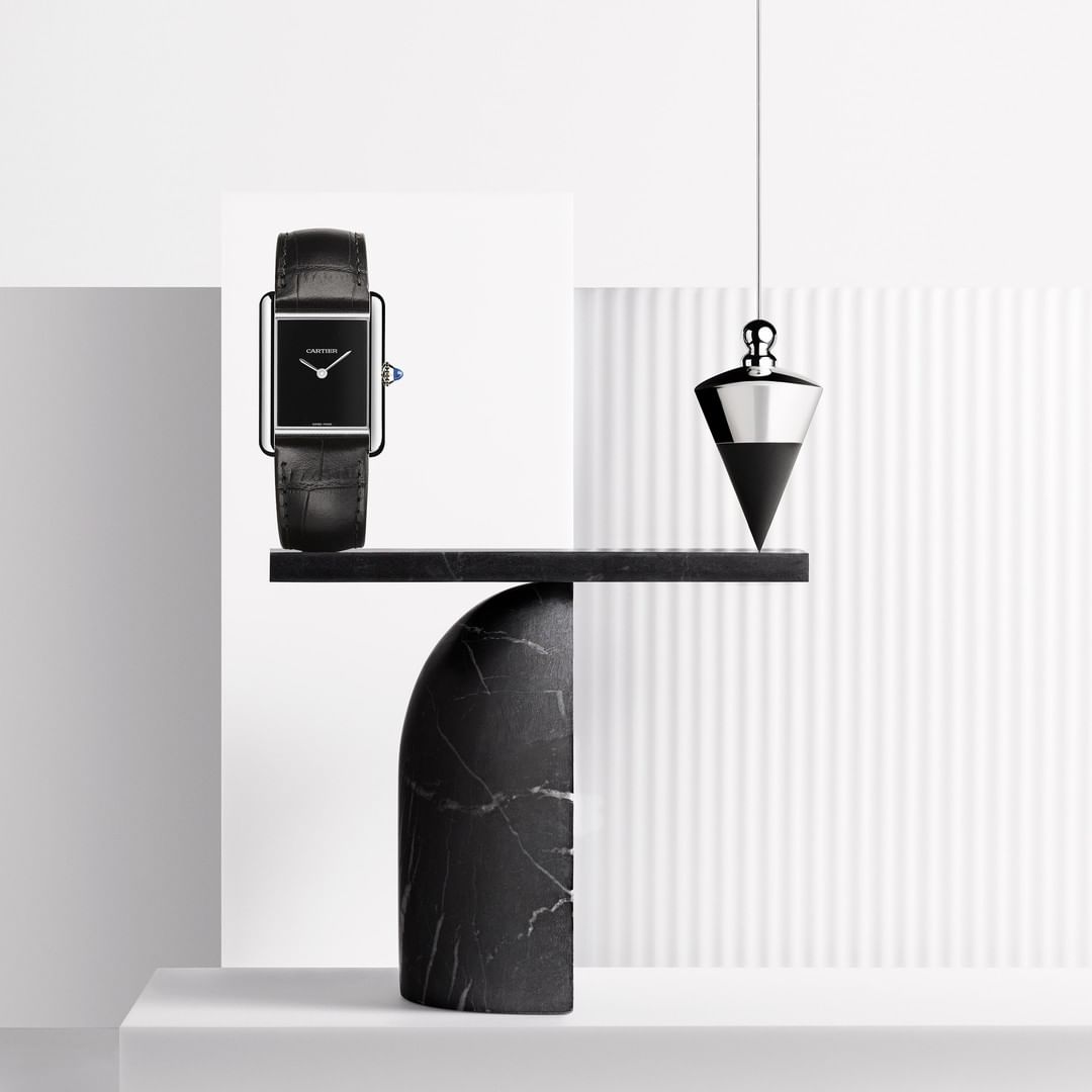 Elegant Longines watch featuring a black leather strap on a marble display stand with a silver plumb bob on a bright white background.