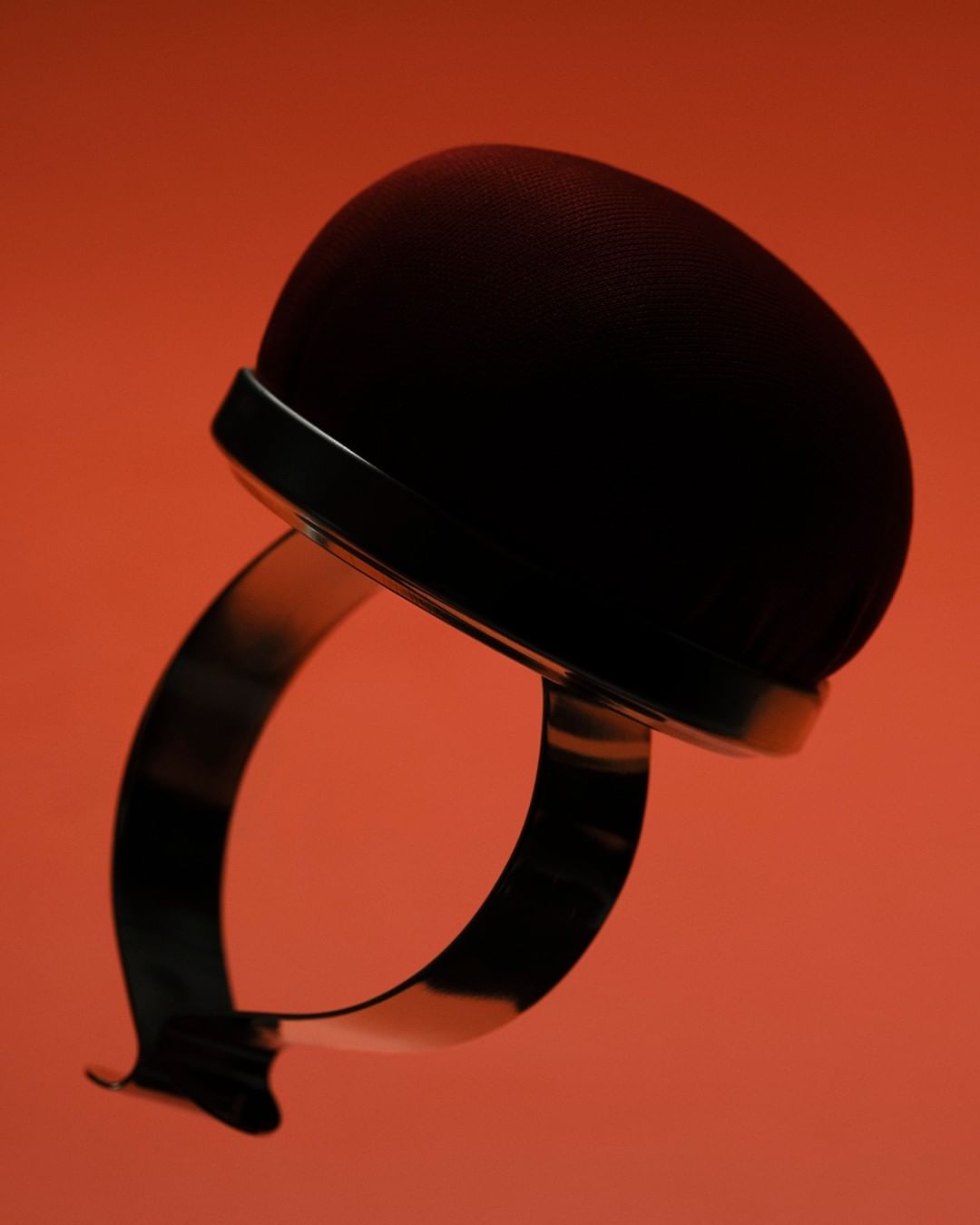 Macro studio shot of a round, maroon pin cushion with metallic silver ring base against a red background, emphasizing texture and design.