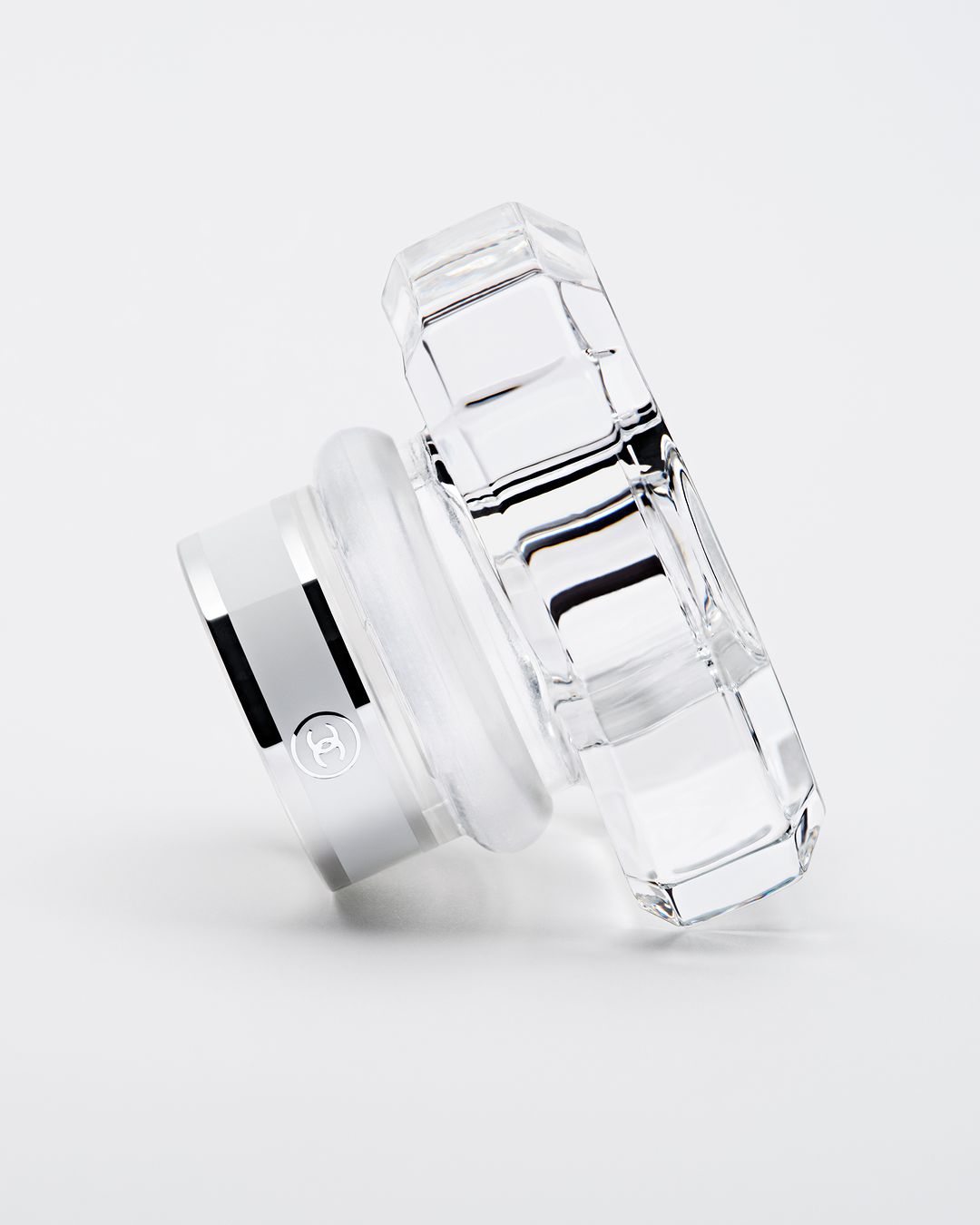Elegant perfume bottle lid, crafted from clear crystal with a silver base, angled view on a clean white surface, product shot.