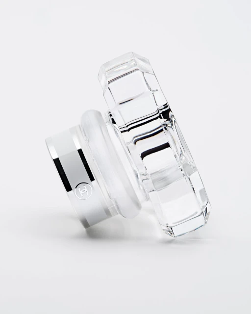 Elegant perfume bottle lid, crafted from clear crystal with a silver base, angled view on a clean white surface, product shot.