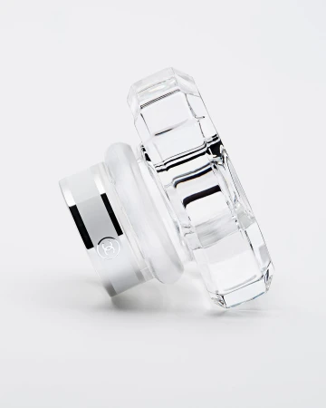 Elegant perfume bottle lid, crafted from clear crystal with a silver base, angled view on a clean white surface, product shot.