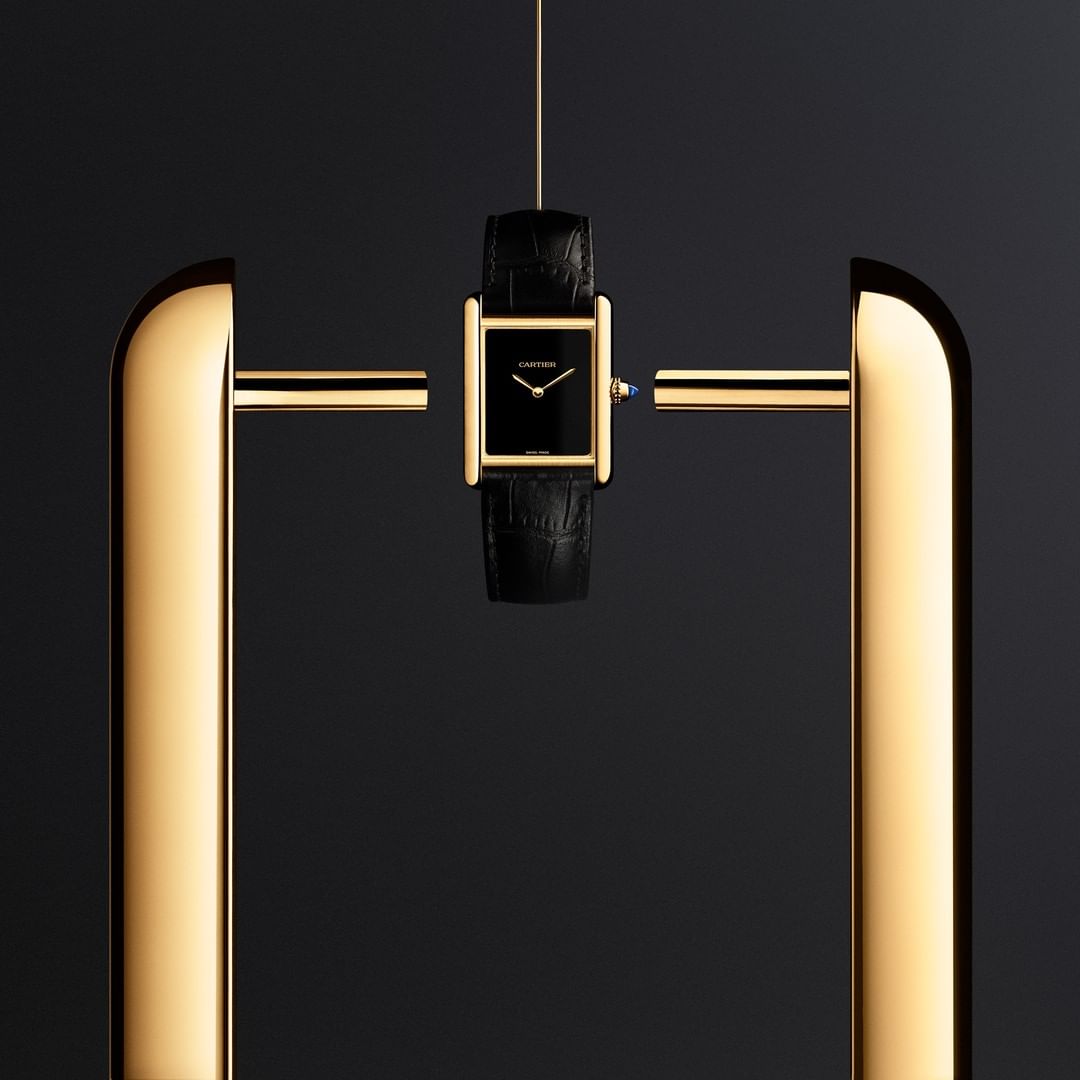 Elegant gold and black Cartier Tank watch suspended between polished gold bars against a dark backdrop. Luxury timepiece, sophistication.