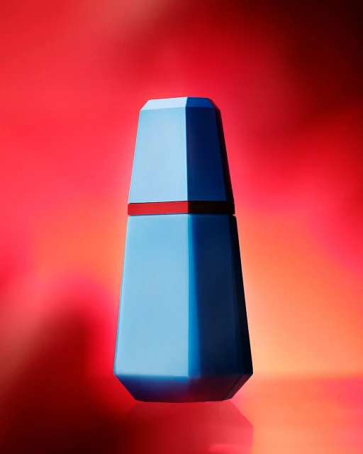 Studio shot of a blue geometric perfume bottle on a reflective surface against a vibrant red and orange gradient background.