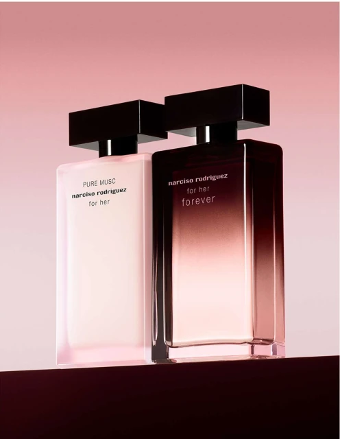 Two Narciso Rodriguez perfume bottles, 'Pure Musc' and 'For Her Forever,' stand on a dark surface against a soft pink backdrop.