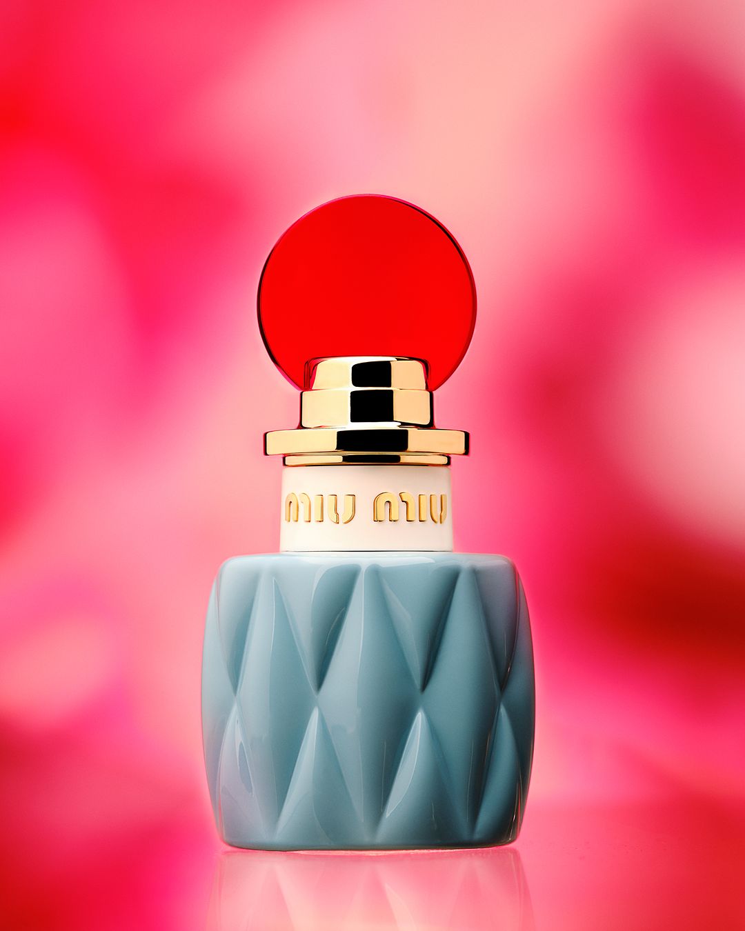 Blue quilted perfume bottle with gold collar and circular red cap against a blurred pink background