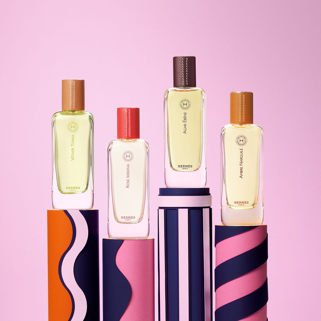 Four Hermès perfume bottles on striped pedestals against a pink background, product photography. Luxury fragrance, beauty product.