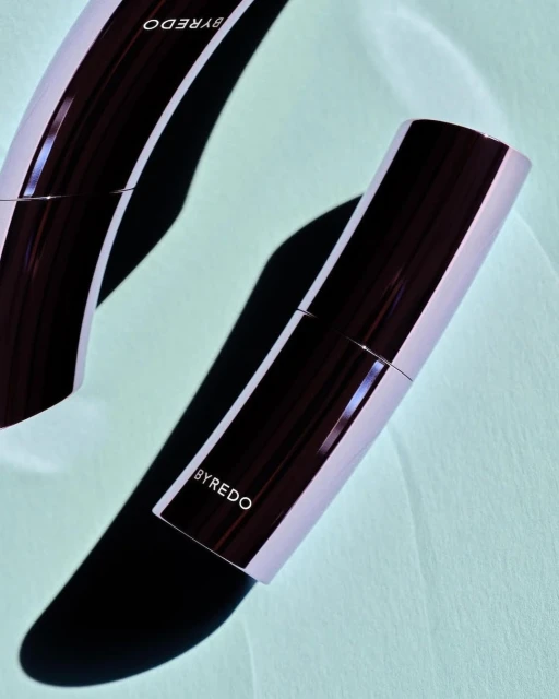 Close-up product shot of two Byredo cosmetic sticks on a light teal surface with soft shadows, emphasizing beauty and minimalist design.