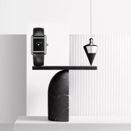 Cartier wristwatch with black leather strap displayed on a sculptural black marble balancing structure with a hanging plumb bob.