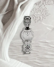 High-end diamond and emerald wristwatch with animal motifs set against a carved white sculptural tree and landscape background.