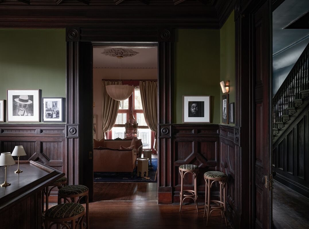 Interior view showcases a stylish living space with dark wood paneling, contrasting green walls, and artistic black-and-white portraits.