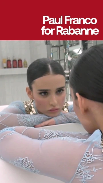 Woman with blue floral lace top looks in mirror. Cosmetics bottles on white shelf. Text "Paul Franco for Rabanne" on top.