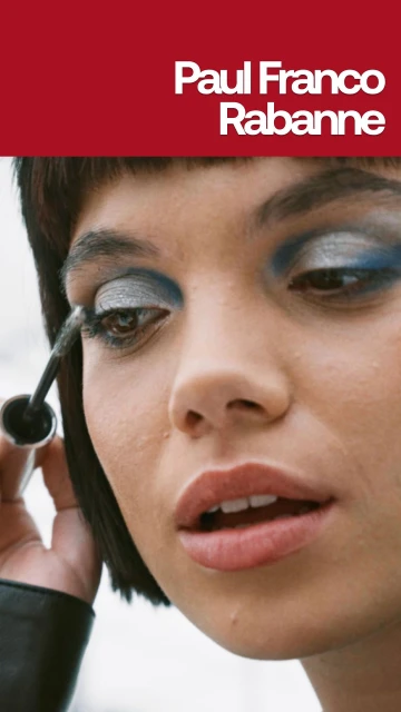 Close-up of a woman applying silver and blue eye makeup with mascara, against a blurred background and Paul Franco Rabanne text.