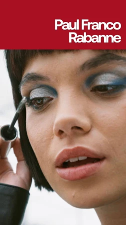 Close-up of a woman applying silver and blue eye makeup with mascara, against a blurred background and Paul Franco Rabanne text.