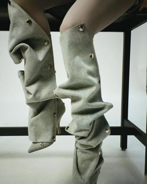 Close-up of a person wearing stylish, loose-fitting, gray leg coverings over high-heeled shoes, captured in a fashion-forward studio setting.