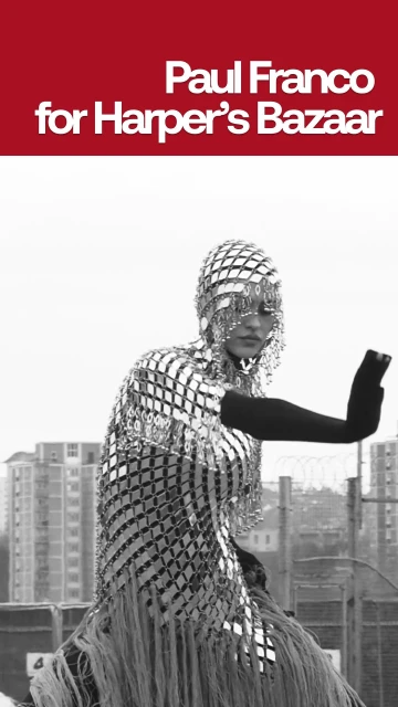 A person posing in a silver beaded outfit with a cityscape in the background for Harper's Bazaar and Paul Franco's work.