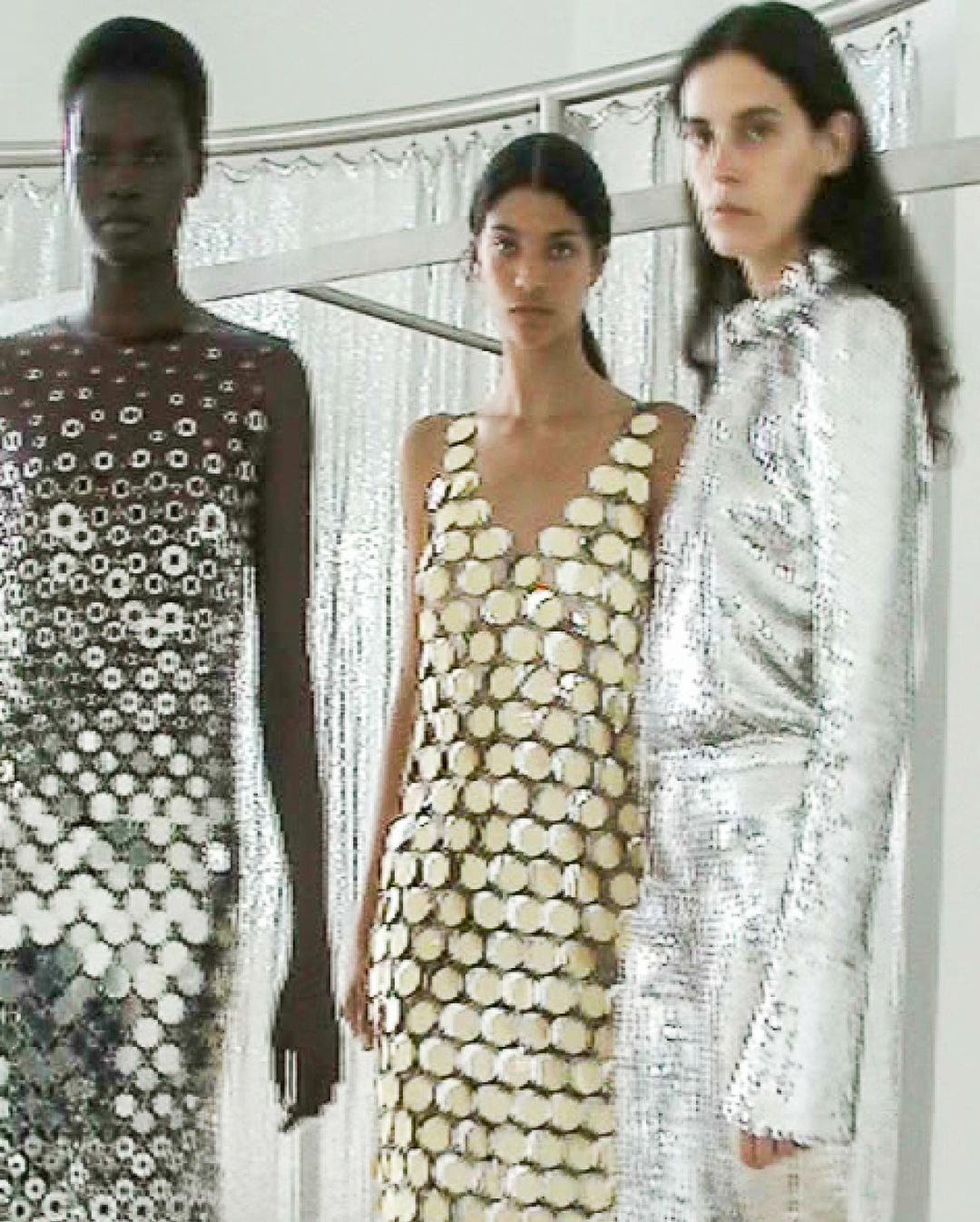 Three fashion models pose in a photo studio, showcasing dresses made of reflective material with unique designs and patterns.