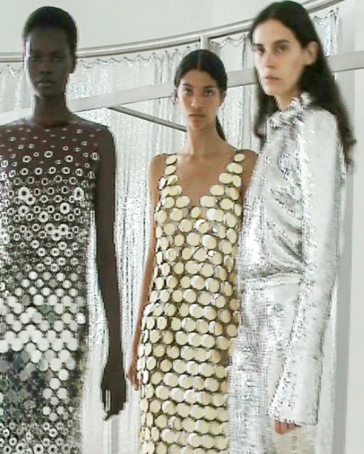 Three fashion models pose in a photo studio, showcasing dresses made of reflective material with unique designs and patterns.