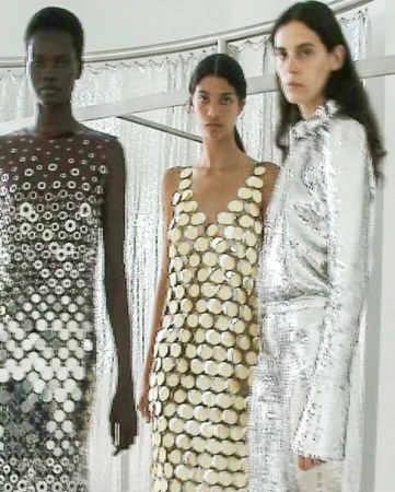 Three fashion models pose in a photo studio, showcasing dresses made of reflective material with unique designs and patterns.