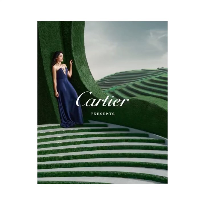 Brunette woman in a navy blue gown poses on green tiered steps in a fashion editorial, with a sky visible in the background.