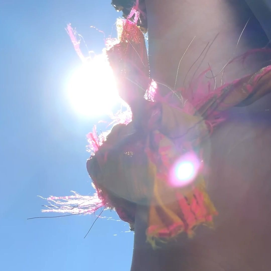 Bright sunlight shines on colorful fabric with fringe, creating a vibrant and eye-catching visual under a clear blue sky.