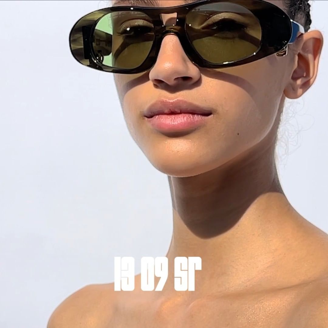 Woman with tan skin wears vintage style sunglasses with brown frames and green lenses in a bright, high key close-up shot.