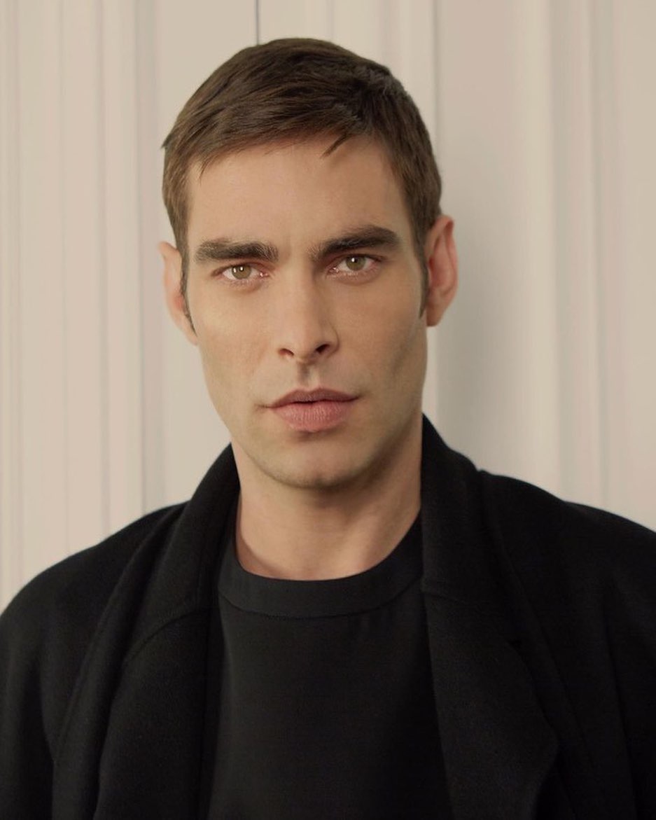 Portrait of an adult male with dark hair and eyes wearing a black shirt and jacket, captured in a photo studio setting with soft lighting.