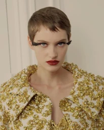 Portrait of a short-haired model wearing a heavily textured gold sequin jacket and dramatic false eyelashes in Paris.