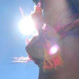 Low-angle shot of a person wearing a fringed pink and yellow garment against a bright sun and blue sky
